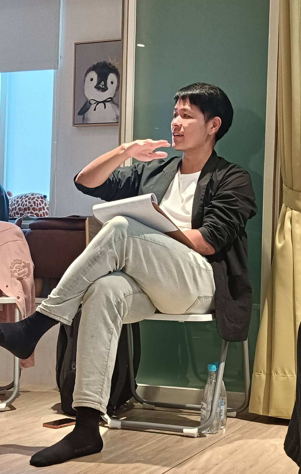 王家齊坐在椅子上，手裡拿著一疊紙，另一手抬起正在說話